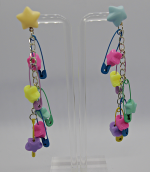 Dangling earrings with pastel star studs and multicolored safety-pin and star charms displayed on a clear stand.