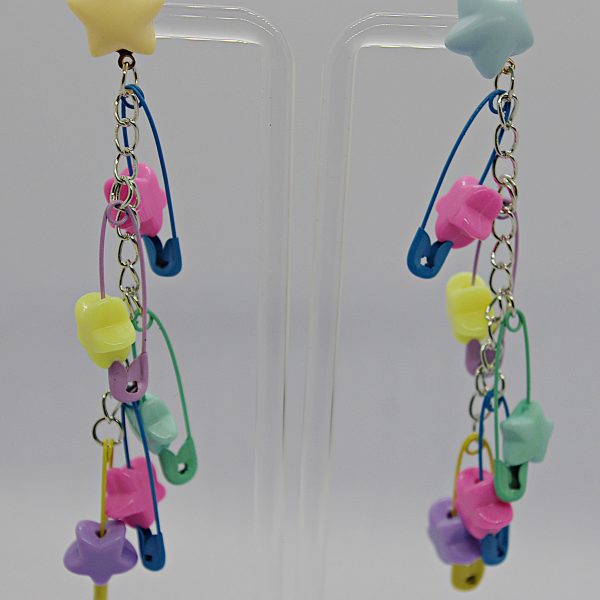 Long pastel star stud earrings with dangling chains of multicolored star charms and tiny safety-pin accents on a clear stand.