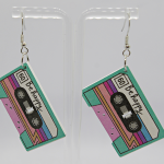 Pair of pastel cassette-tape earrings reading Be happy with teal, pink and purple stripes, on silver hooks on a clear stand.