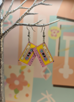 Pink-yellow cassette earrings labeled Best of the 80s hang from a silver tree against a pastel backdrop.