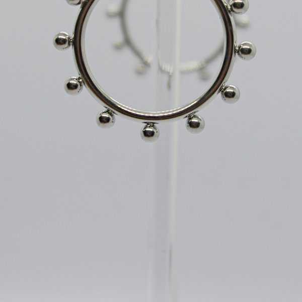 Silver hoop earring with small round beads evenly spaced around it, displayed on a clear stand against a pale background.