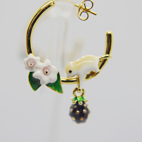Gold hoop earring with enamel white bird perched by two white flowers and green leaves, dangling dark beaded berry charm.