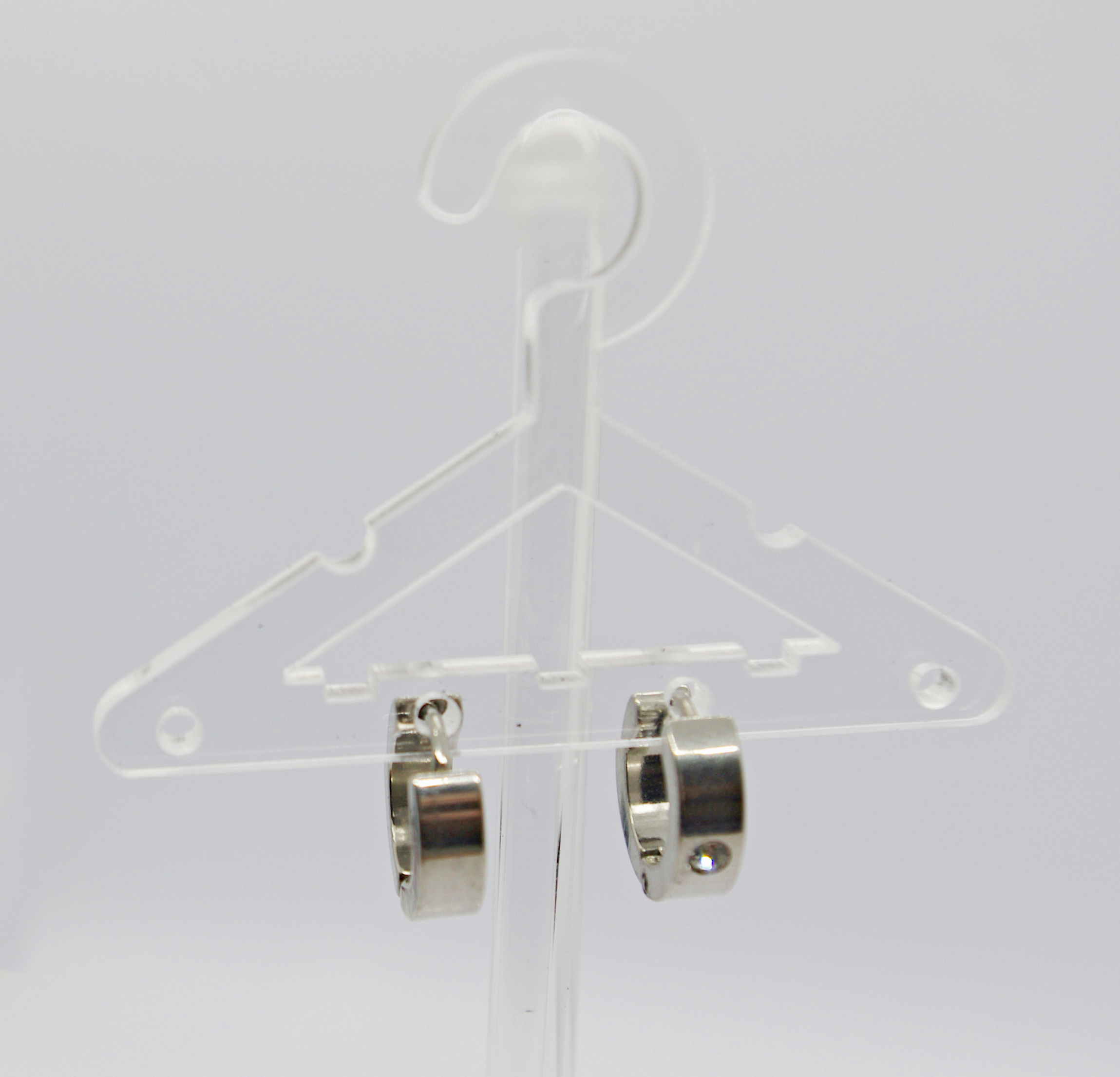Clear plastic miniature hanger displaying a pair of small silver hoop earrings against a white background.