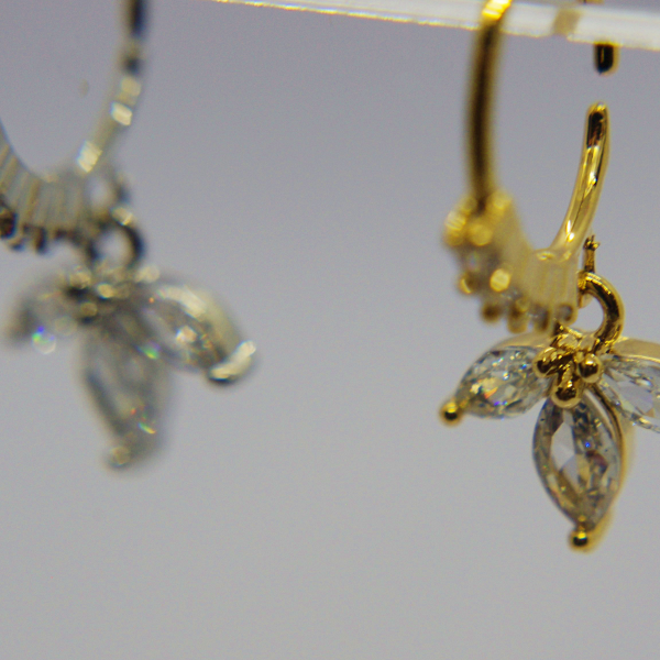 Gold hoop nose ring with three marquise-cut clear stones arranged like a small flower, with a blurred silver earring in the background