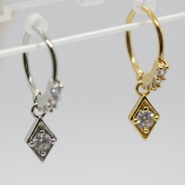 Two hoop earrings, one silver and one gold, each with a diamond-shaped charm set with a round clear stone.