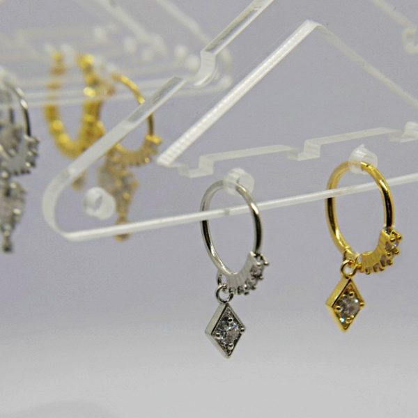 Small silver and gold hoop earrings with diamond-shaped crystal pendants hanging from a clear acrylic display.