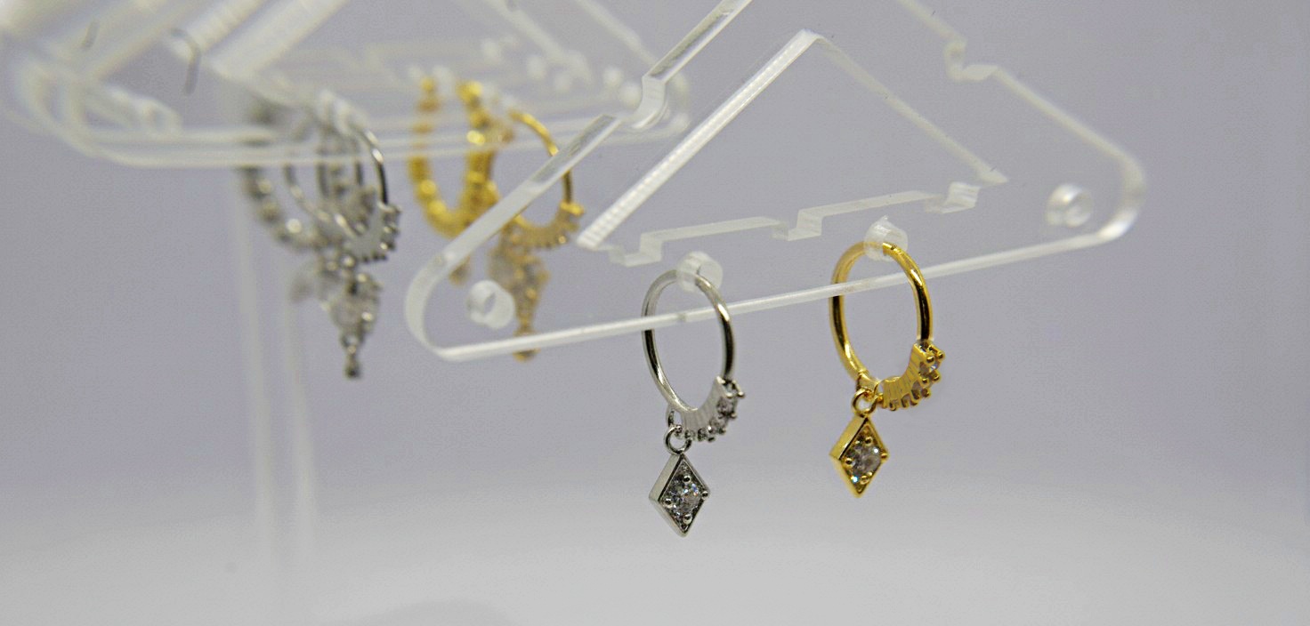 Small silver and gold hoop earrings with diamond-shaped crystal pendants hanging from a clear acrylic display.