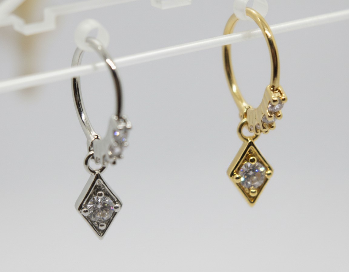 Two hoop earrings, one silver and one gold, each with a diamond-shaped charm set with a round clear stone.