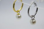 Two small hoop earrings, one gold and one silver, each with a single dangling white pearl against a light background.