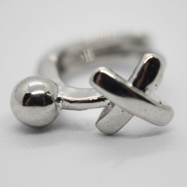 Silver ring with a polished spherical end and an X-shaped end resting on a white surface.