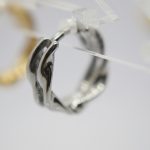 Small silver twisted hoop earring hanging on a clear acrylic display, with a blurred gold hoop behind.