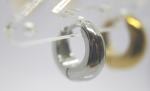 Small chunky silver hoop earring in close-up on a clear plastic display with a blurred gold hoop behind it.