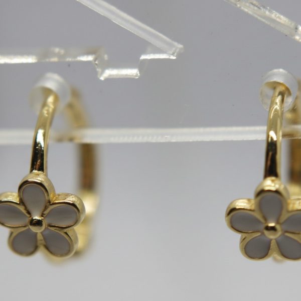 Pair of gold hoop earrings each featuring a white-enamel five-petal flower charm on a clear display