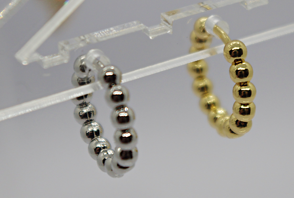 Two beaded hoop earrings, one silver and one gold, hanging from a clear acrylic display.