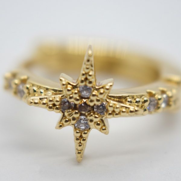 Close-up of a gold ring with a starburst centerpiece studded with small clear stones on a white background.