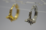 Small silver hoop earring with a beaded, cross-shaped decorative cluster in focus, blurred gold hoop visible behind.