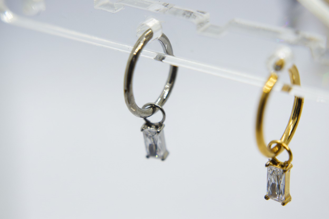 Two small hoop earrings on a clear display: silver and gold hoops each dangling a small rectangular clear stone.