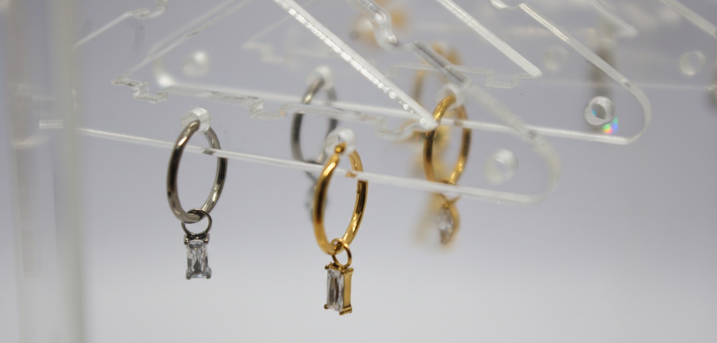 Silver and gold small hoop earrings hanging on a clear acrylic rack, each with a rectangular baguette-cut drop stone.