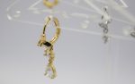 Gold hoop earring with dangling baguette and pear-shaped clear stones hanging from a transparent acrylic display