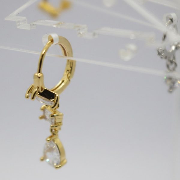 Gold hoop earring with dangling baguette and pear-shaped clear stones hanging from a transparent acrylic display