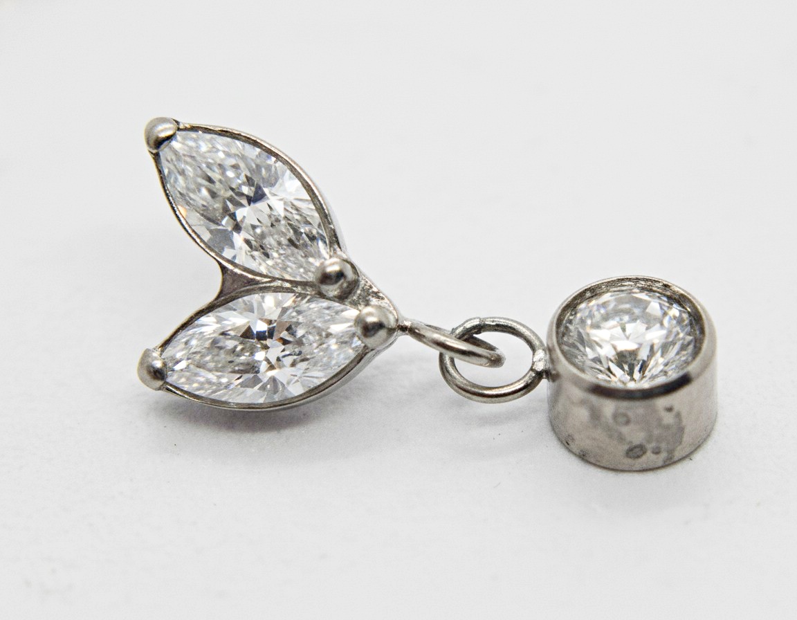 Silver pendant with two marquise-cut diamonds arranged like leaves and a round bezel-set diamond linked by a small ring.