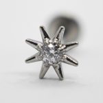 Close-up of an eight-point silver star stud with a central clear faceted gem against a soft white background.
