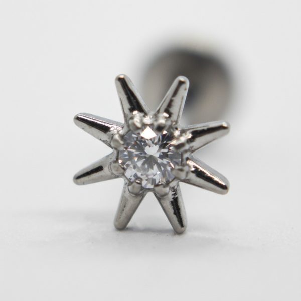Close-up of an eight-point silver star stud with a central clear faceted gem against a soft white background.