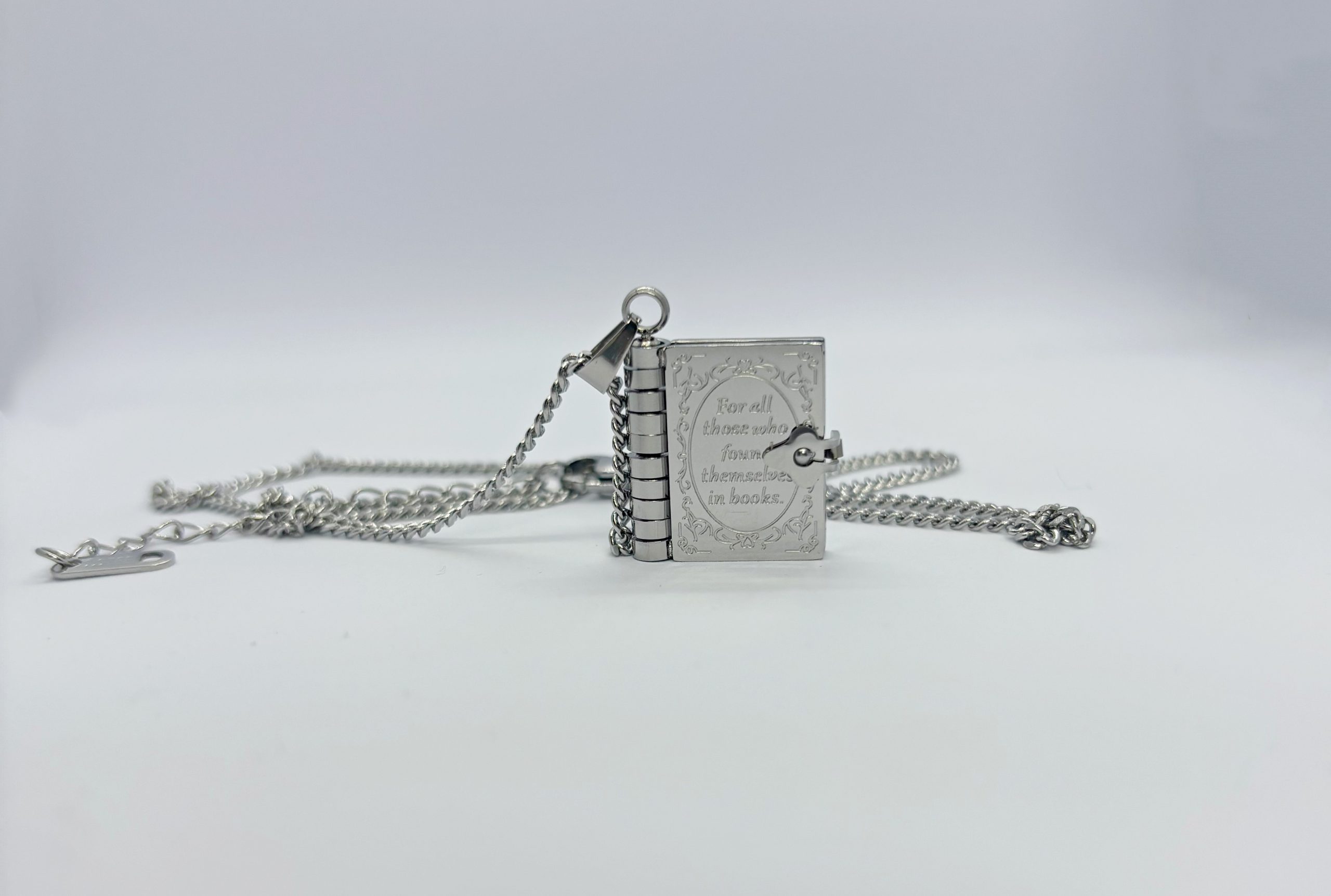Silver book locket pendant on a chain engraved "For all those who found themselves in books," on a white background.