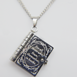 Silver book locket pendant engraved For all those who found themselves in books, hanging from a silver chain on a plain white background.