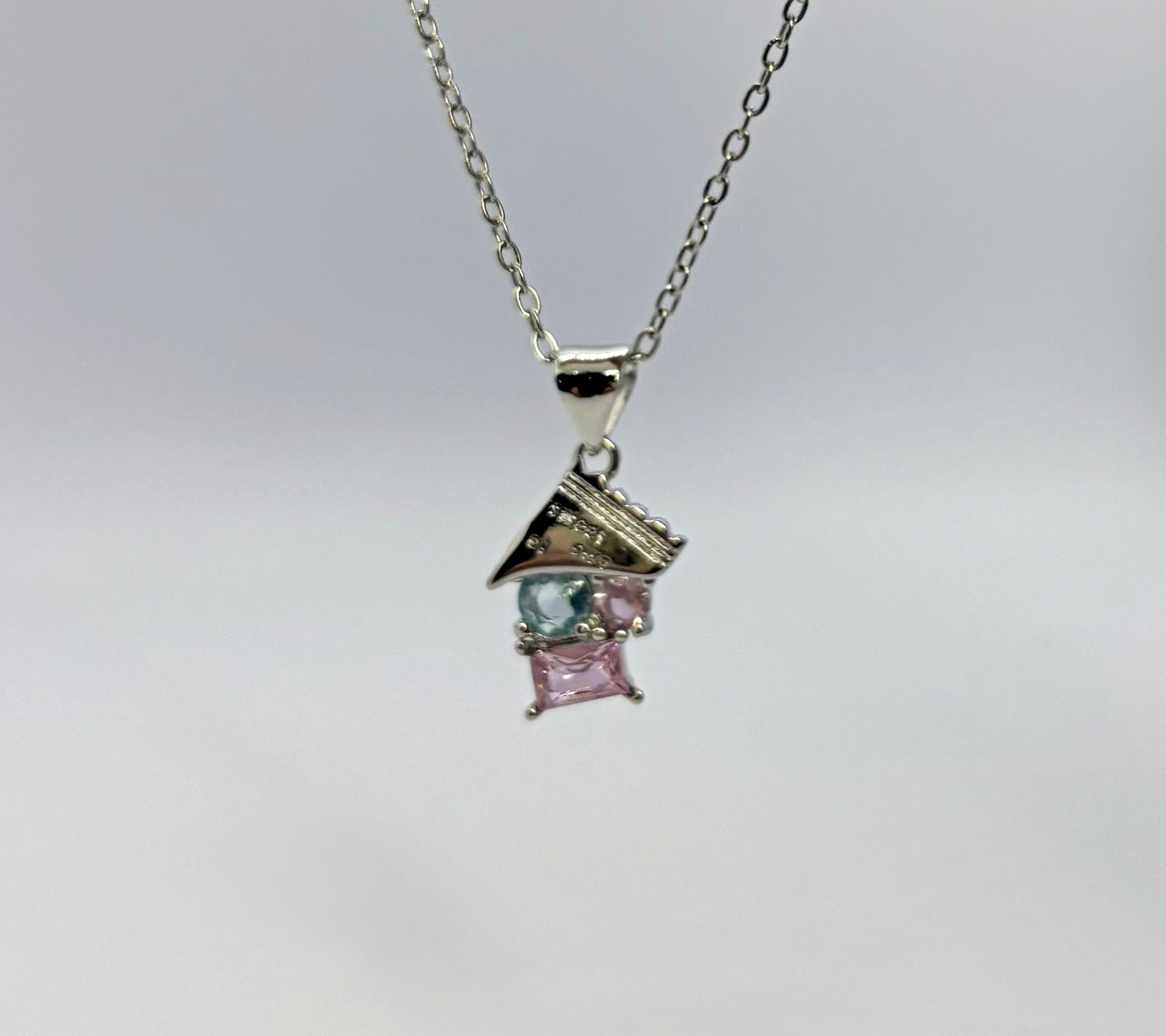 Silver necklace pendant with a textured triangular cap above a pale blue round stone and a pink square stone