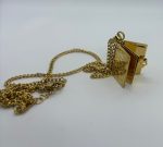 Gold chain necklace with a small open book-shaped locket pendant featuring an ornate cover, chain slightly tangled on a white background.