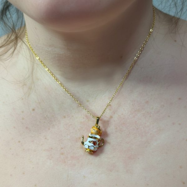Gold chain necklace with a small white-and-gold teapot pendant resting on a bare neck and upper chest.
