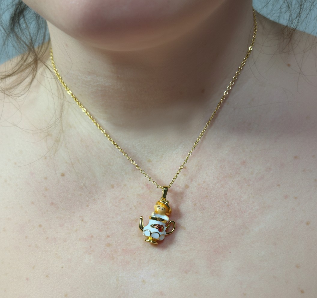 Gold chain necklace with a small white-and-gold teapot pendant resting on a bare neck and upper chest.