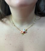 Gold chain necklace with a pink enamel flower, tiny white rabbit charm and green jeweled accents resting on a bare collarbone.
