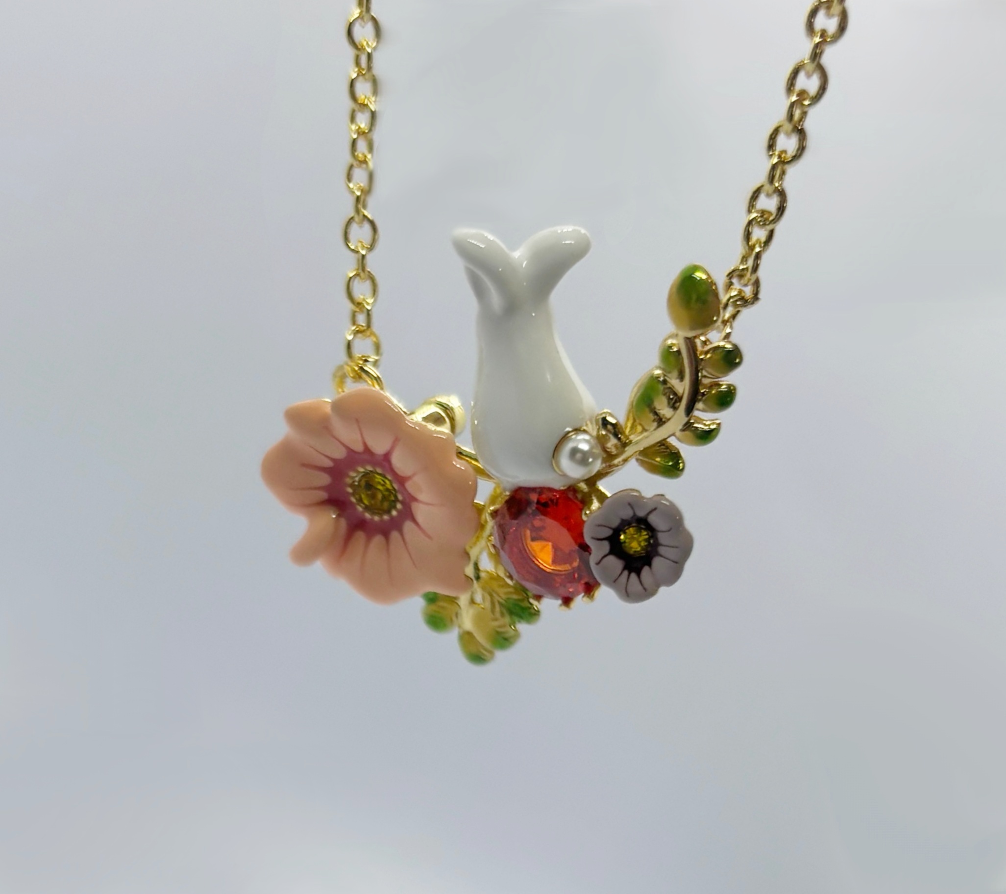 Gold chain pendant featuring a white tail-shaped charm with peach and gray enamel flowers, red gem, pearl, and green leaves.