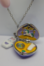 Open heart-shaped enamel locket pendant with a tiny unicorn carousel scene and yellow inner compartment on a silver chain.