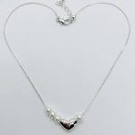 Delicate silver chain necklace shaped like a heart with a polished silver heart pendant flanked by white pearls and a lobster clasp