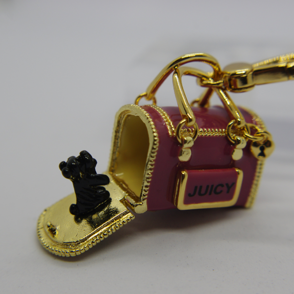 Pink and gold miniature handbag keychain with JUICY plaque, open flap and a tiny black dog figurine, attached to a gold clasp.