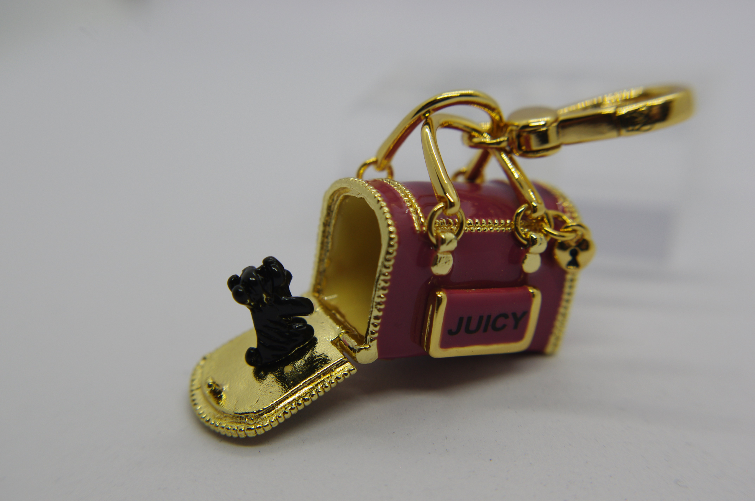 Pink and gold miniature handbag keychain with JUICY plaque, open flap and a tiny black dog figurine, attached to a gold clasp.