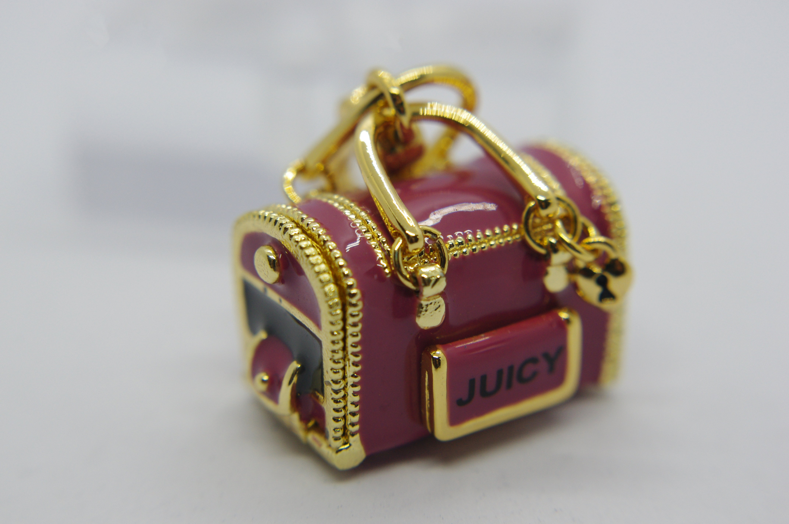 Miniature glossy pink handbag charm with gold hardware and zipper details, front plate labeled "JUICY".