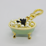 Mini mint-green clawfoot bathtub charm with gold legs and clasp, filled with faux pearls and a small black paw sticking up.