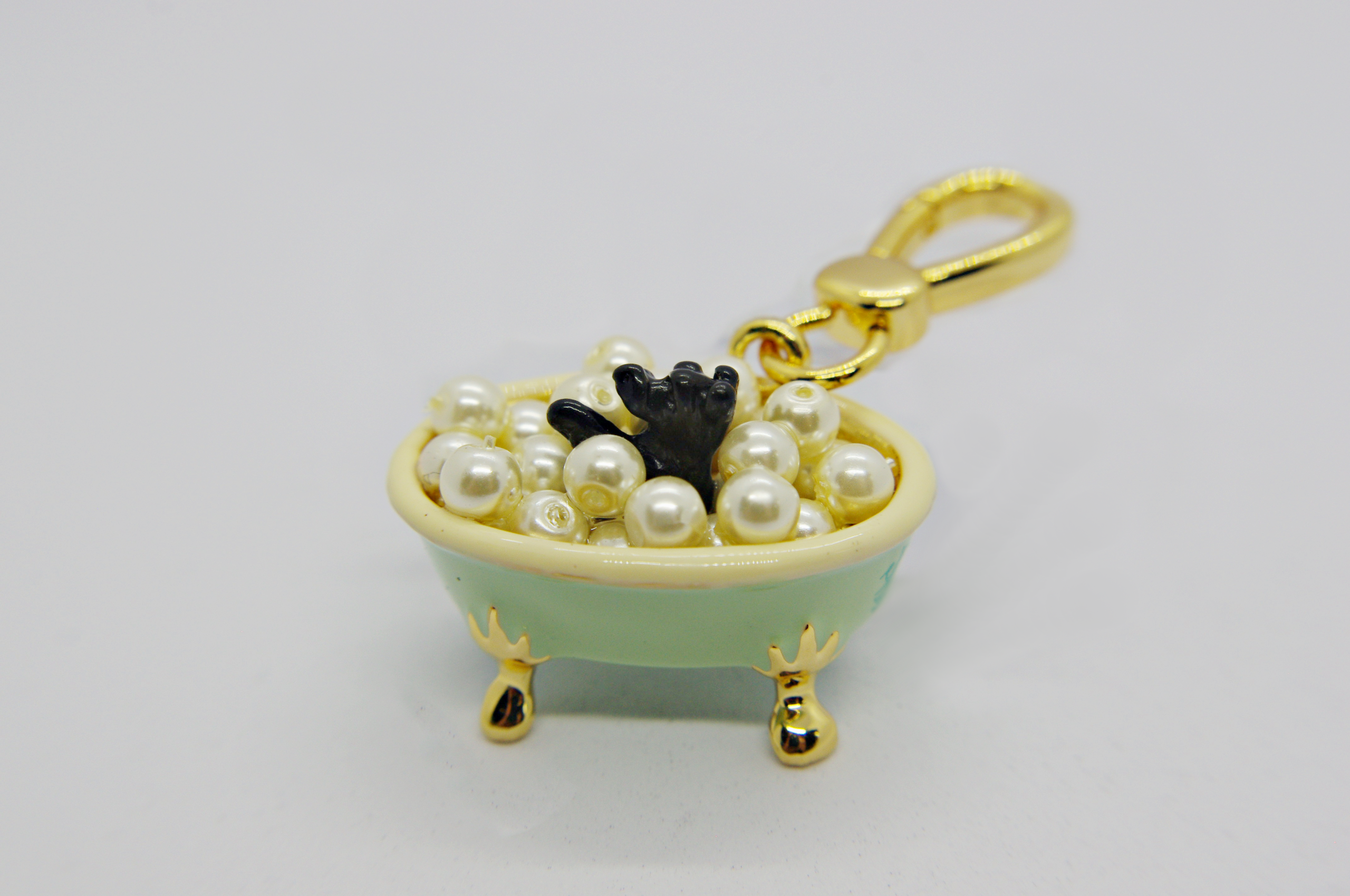 Mini mint-green clawfoot bathtub charm with gold legs and clasp, filled with faux pearls and a small black paw sticking up.