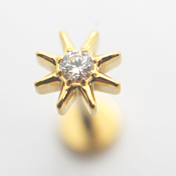 Close-up of a gold eight-point star stud earring with a central round clear gemstone on a soft gray background.