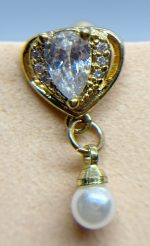 Close-up of a gold earring with a clear teardrop stone and dangling pearl