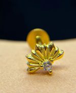 Close-up of a small gold flower-shaped earring with a clear gemstone stud on skin against a dark background