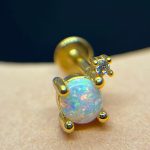 Close-up of a gold stud earring with a round opal showing blue-pink flashes and a small prong-set diamond accent
