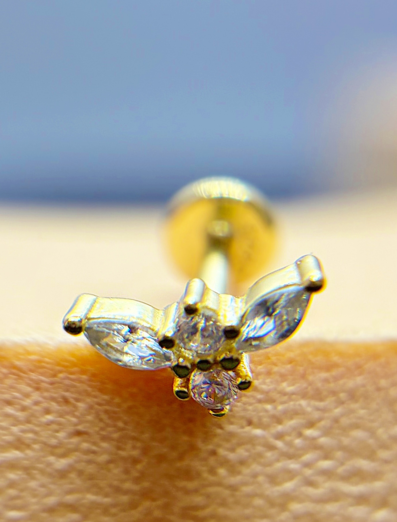 Close-up of a diamond stud earring on skin with a blurred blue background
