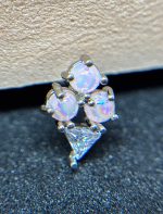 Cluster of three small round opal stones and one triangular clear gem set in silver on a textured dark surface.