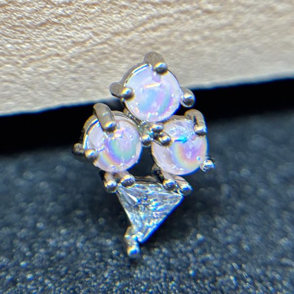 Cluster of three small round opal stones and one triangular clear gem set in silver on a textured dark surface.