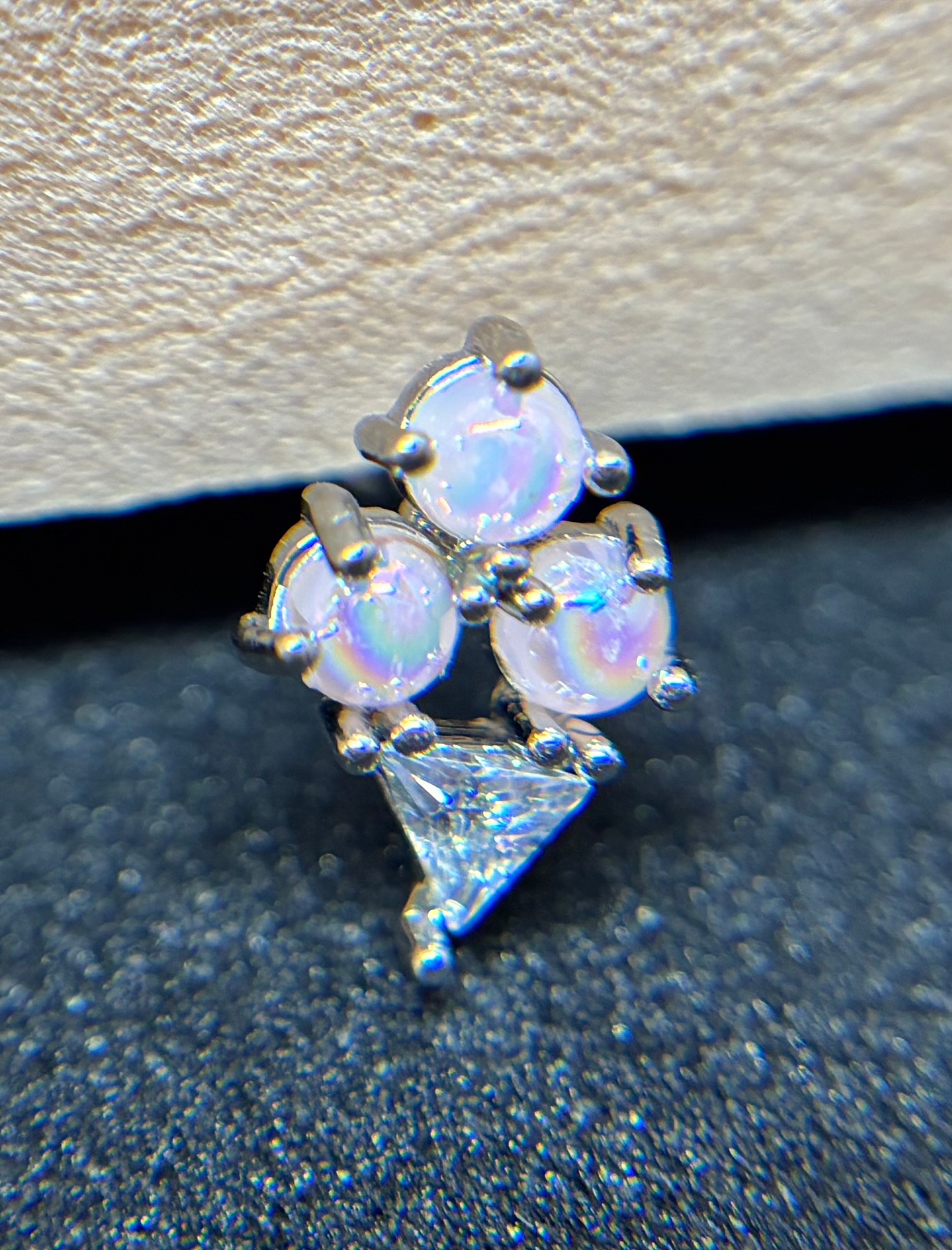 Cluster of three small round opal stones and one triangular clear gem set in silver on a textured dark surface.